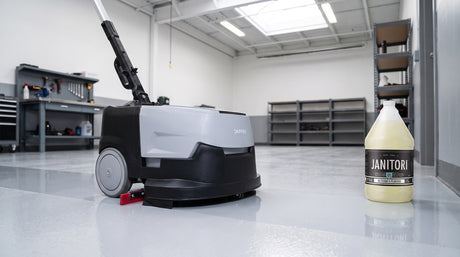Compact commercial auto scrubber cleaning a glossy gray epoxy floor in a service bay beside a JANITORI Floor Cleaner No.61 jug