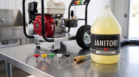 Red, yellow, green, white and black pressure washer nozzle tips lined up on a steel workbench beside a wand coupler, gas pressure washer and JANITORI Degreaser MAX No.72 jug